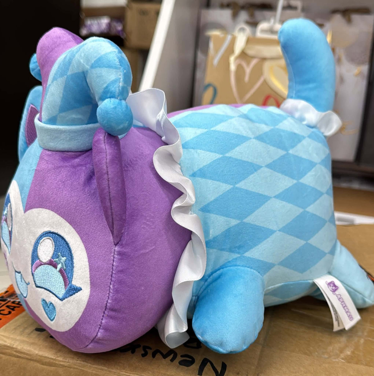 Side view of Jester Cat plush showing blue diamond-patterned body, white ruffled collar and raised tail