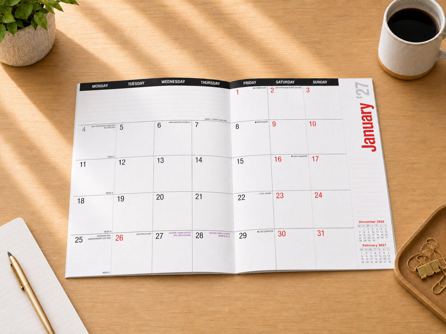 2027 Everyday Planner Black open on desk showing January 2027 month view with coffee and stationery