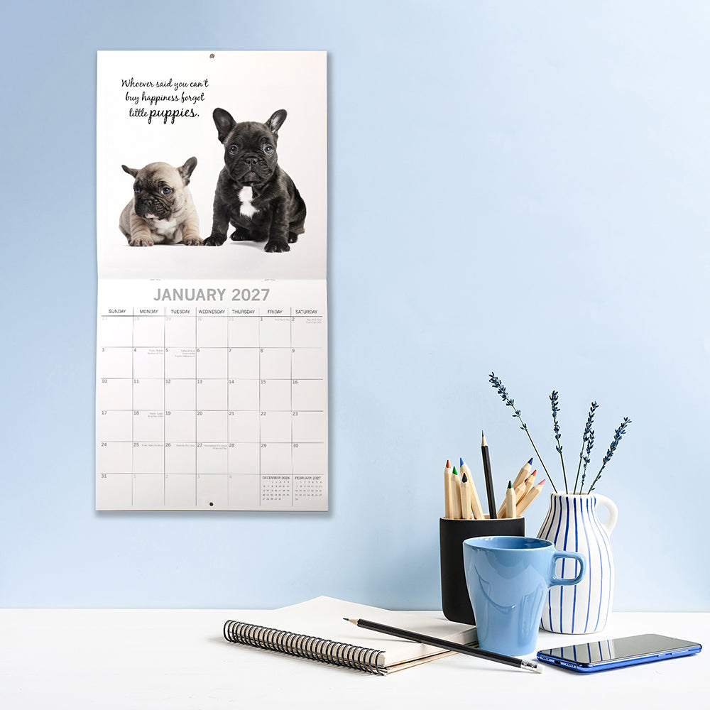 Adorable Dogs 2027 Calendar - lifestyle shot on desk showing January 2027 page with two French Bulldog puppies on white background with puppy quote