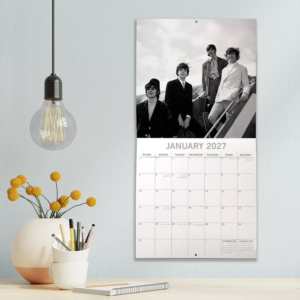 The Beatles 2027 Square Wall Calendar – January 2027 lifestyle shot featuring a black and white photo of The Beatles descending aircraft steps displayed on a modern wall