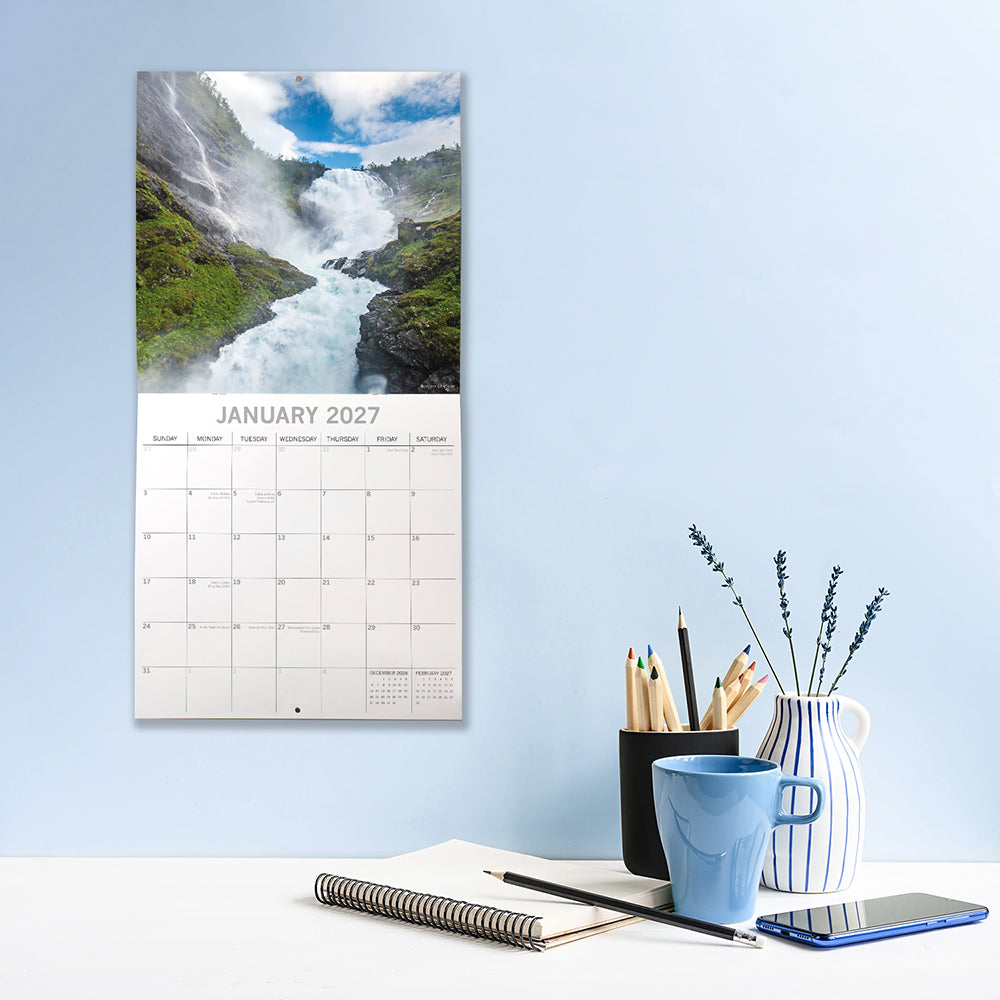 Waterfalls 2027 Calendar – January 2027 lifestyle shot on blue wall above desk featuring raging white torrent of Kjøsfossen waterfall in Norway under bright blue sky