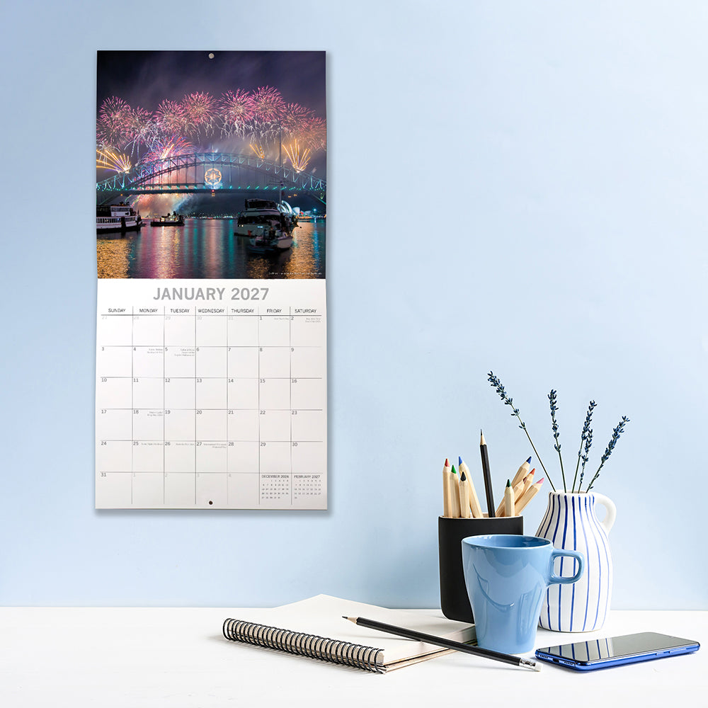 Landmarks of Australia 2027 Square Wall Calendar - January 2027 lifestyle shot hung on wall above a home office desk featuring Sydney Harbour Bridge New Year fireworks