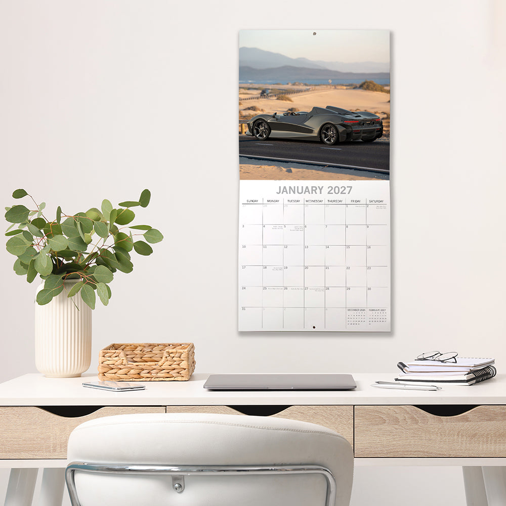 Super Cars 2027 Square Wall Calendar - January 2027 lifestyle shot hung on wall above a styled home office desk featuring a grey Corvette convertible on a desert road