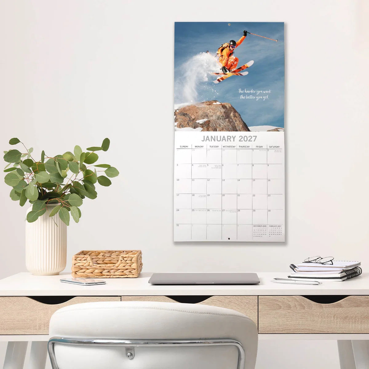 Motivation 2027 Square Wall Calendar – January 2027 lifestyle shot featuring a skier launching off a mountain peak displayed on a home office wall