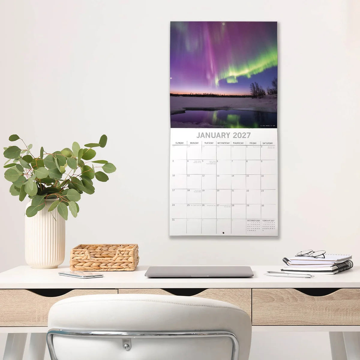 Natural Wonders 2027 Square Wall Calendar – January 2027 lifestyle shot featuring the Northern Lights aurora borealis over a frozen lake displayed on a home office wall