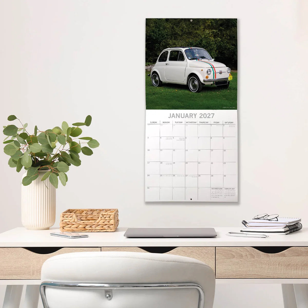Classic Cars 2027 Square Wall Calendar - January 2027 lifestyle shot hung on wall above a styled home office desk featuring a white Fiat 500 with Italian flag stripe